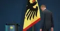 Friedrich Merz odwrócony tyłem obok flagi z godłem Niemiec