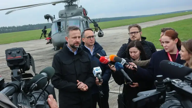 Władysław Kosiniak-Kamysz odpowiada na pytania dziennikarzy na płycie lotniska. W tle śmigłowiec