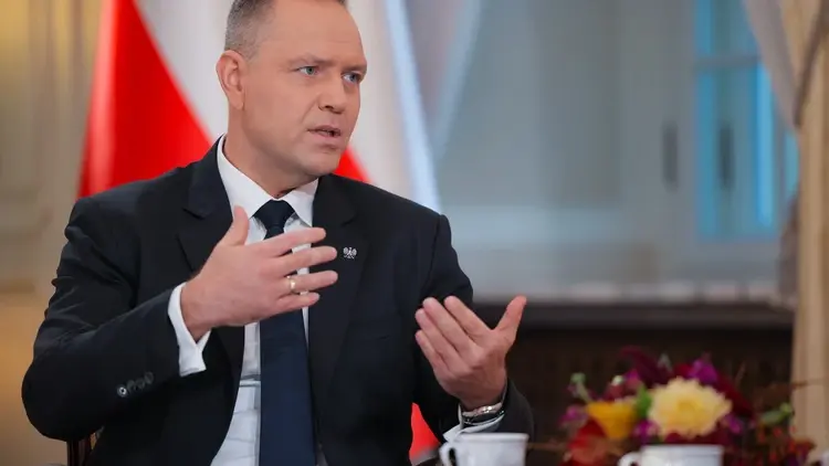 Karol Nawrocki gestykuluje, w tle flaga Polski