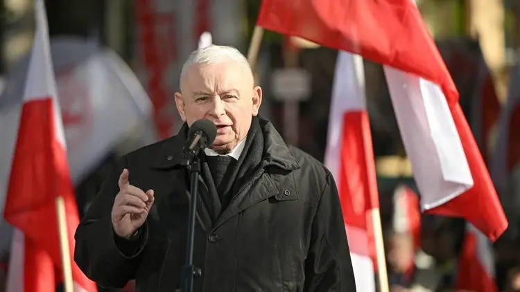 Jarosław Kaczyński przemawia i gestykuluje, w tle polskie flagi