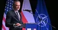 Szef BBN Bartosz Grodecki przemawia do mikrofonu. W tle flaga USA, Polski i NATO