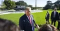 Donald Trump rozmawia z dziennikarzami. W tle trawnik i śmigłowiec