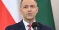 Karol Nawrocki przemawia do mikrofonu, w tle flaga Polski
