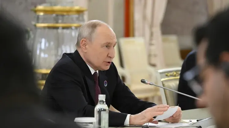 Władimir Putin przemawia do mikrofonu siedząc przy stole