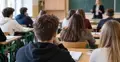 Chłopak siedzący tyłem na lekcji. W tle nauczyciel i uczniowie
