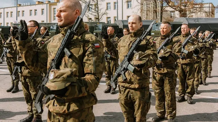 Żołnierze WOT w mundurach z karabinami, w tle bloki mieszkalne