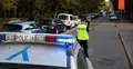 Funkcjonariusz policji, na pierwszym planie radiowóz w tle przejście dla pieszych i zaparkowane samochody
