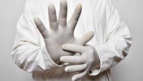 Osoba w fartuchu naciągająca rękawice lekarskie