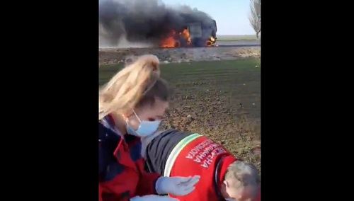 Ratownicy medyczni usiłują pomoc rannemu. W tle płonie karetka