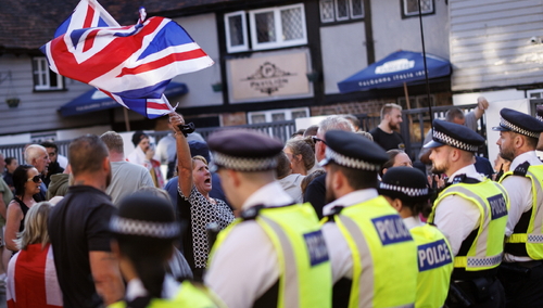 Kontrmanifestanci machają flagą, gromadząc się przed hotelem TLK Apartments, w którym przebywają osoby ubiegające się o azyl