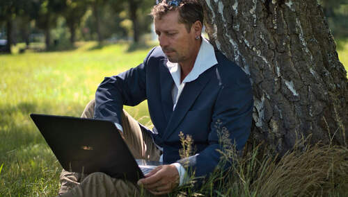 Mężczyzna z laptopem siedzi pod drzewem