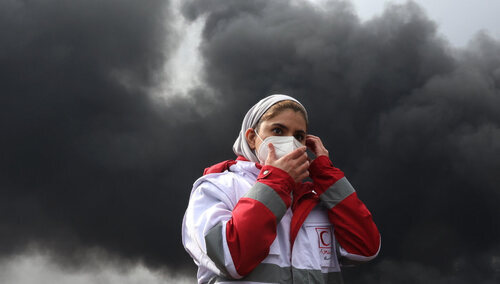 Przedstawicielka Czerwonego Półksiężyca na tle dymu z płonącej irańskiej rafinerii