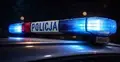 Radiowóz policji z włączonymi niebieskimi i czerwonymi światłami na dachu nocą, widoczny napis „POLICJA” na belce świetlnej.
