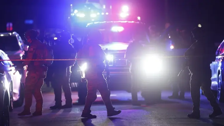 Uzbrojeni agenci FBI przed domem podejrzanego, w tle radiowóz policyjny na sygnale