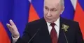 Władimir Putin przemawia gestykulując na tle rosyjskich flag