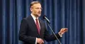 Zbigniew Bogucki w garniturze gestykuluje przemawiając do mikrofonu