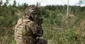 Żołnierz NATO w kamuflażu prowadzi ogień podczas ćwiczeń wojskowych w terenie leśnym