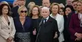 Jarosław Kaczyński przemawia do mikrofonu i gestykuluje. Wokół stoją ludzie