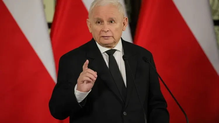 Jarosław Kaczyński przemawia i gestykuluje na tle polskich flag