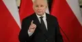 Jarosław Kaczyński przemawia i gestykuluje na tle polskich flag