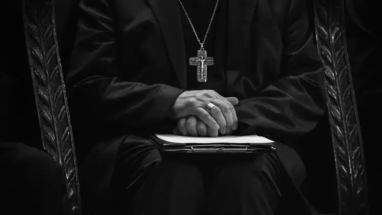hierarcha kościelny siedzący z rękami złożonymi na kolanach