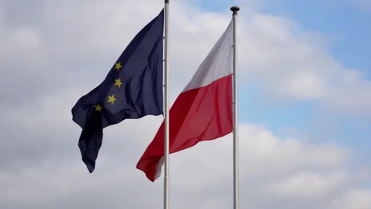 Flagi Polski i Unii Europejskiej na masztach na tle zachmurzonego nieba