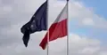 Flagi Polski i Unii Europejskiej na masztach na tle zachmurzonego nieba