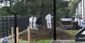 Trzy osoby w białych kombinezonach kopią w ziemi na prywatnej posesji
