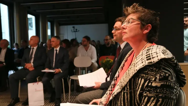 Hanna Radziejowska trzyma kartki papieru, w tle sala wykładowa i dwóch mężczyzn w garniturach