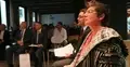 Hanna Radziejowska trzyma kartki papieru, w tle sala wykładowa i dwóch mężczyzn w garniturach