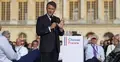 Emmanuel Macron przemawia do mikrofonu na zgromadzeniu. W tle siedzący ludzie