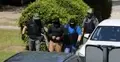 Policjanci prowadzą skutego kajdankami mężczyznę podczas zatrzymania.