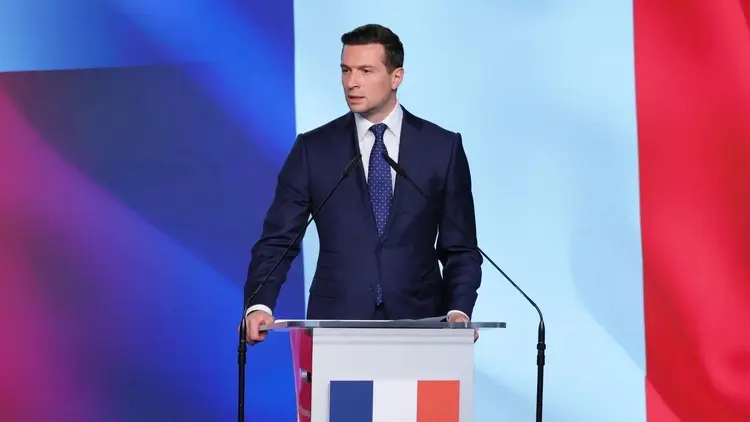 Jordan Bardella przemawia na konferencji prasowej. W tle francuskie barwy narodowe