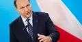 Radosław Sikorski przemawia i gestykuluje. W tle polska flaga