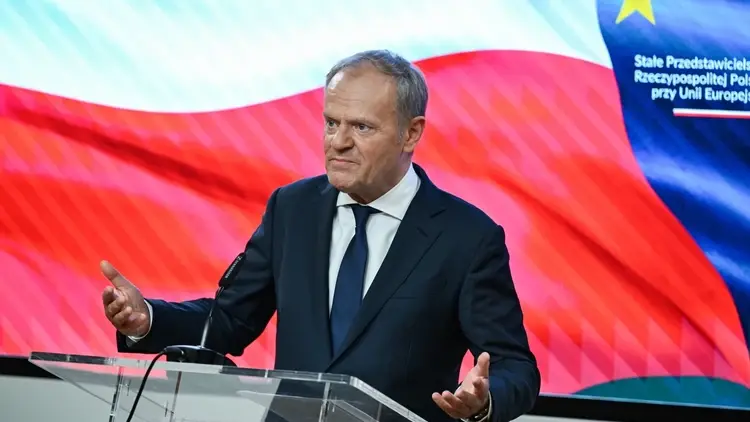 Donald Tusk przemawia na konferencji prasowej. W tle polska flaga