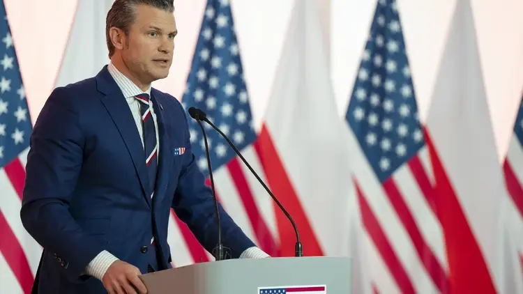 mężczyzna w garniturze stojący na tle flag Polski i USA