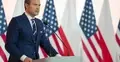 mężczyzna w garniturze stojący na tle flag Polski i USA