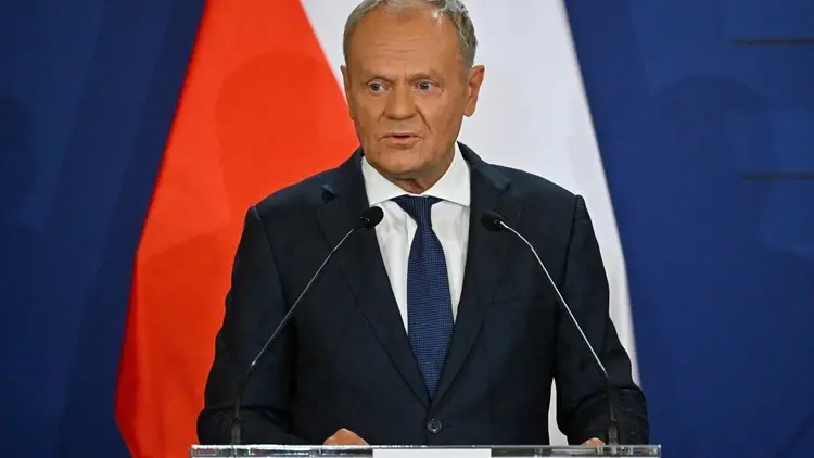 Donald Tusk przemawia do mikrofonu. W tle polska flaga
