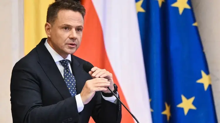 Rafał Trzaskowski trzyma mikrofon. W tle flaga Polski i UE