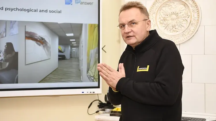 Andrij Sadowy w ciemnej bluzie gestykuluje. W tle ekran z prezentacją