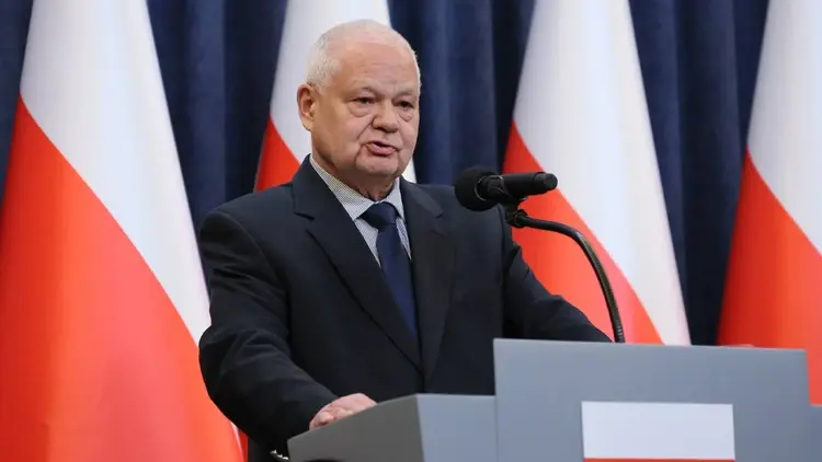 Adam Glapiński na tle polskich flag mówi do mikrofonu