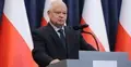 Adam Glapiński na tle polskich flag mówi do mikrofonu