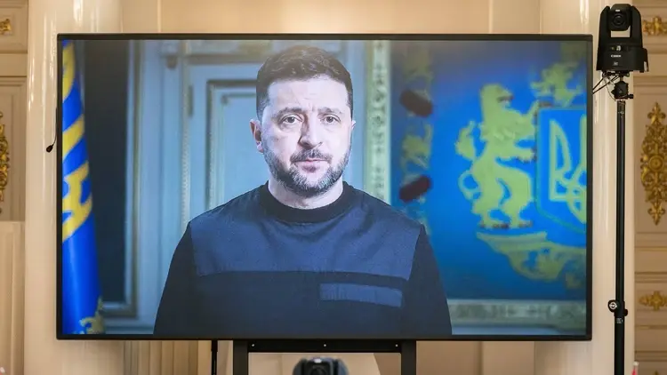 Prezydent Ukrainy Wołodymyr Zełenski podczas telewizyjnego wystąpienia na ekranie, na tle ukraińskich symboli państwowych