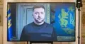 Prezydent Ukrainy Wołodymyr Zełenski podczas telewizyjnego wystąpienia na ekranie, na tle ukraińskich symboli państwowych