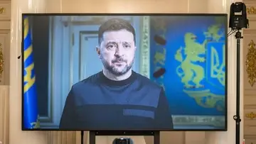 Prezydent Ukrainy Wołodymyr Zełenski podczas telewizyjnego wystąpienia na ekranie, na tle ukraińskich symboli państwowych