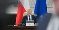 Donald Tusk siedzi przy biurku. W tle flaga Polski i UE