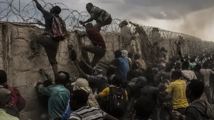Migranci szturmujący mur z zasiekami z drutu kolczastego