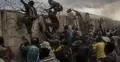 Migranci szturmujący mur z zasiekami z drutu kolczastego