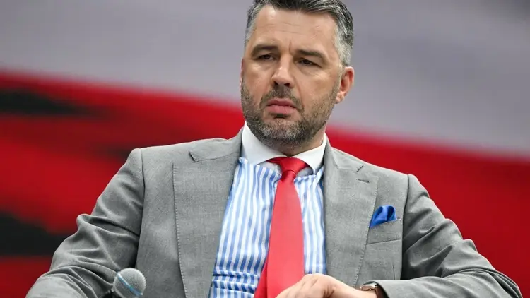 Michał Rachoń z mikrofonem na tle ekranu z biało-czerwoną flagą