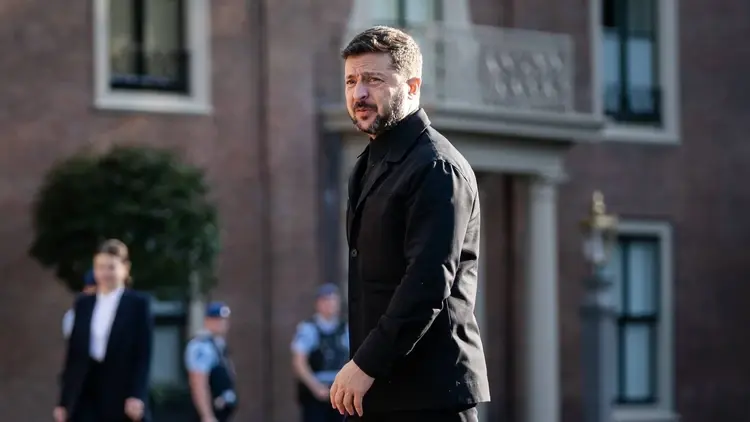 Wołodymir Zełenski w czarnym garniturze idzie. W tle budynek i policja